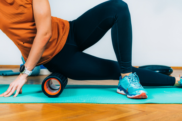 A runner lying on a yoga mat with a foam roller beneath them.