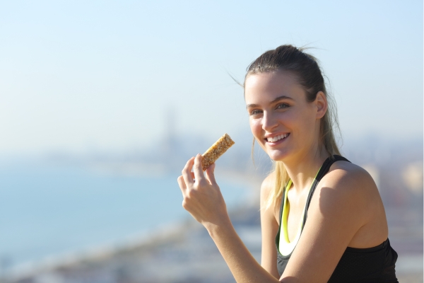 A smiling runner enjoying a granola bar in a sunny tropical environment, highlighting the role of proper nutrition in recovery and performance.