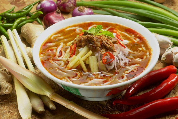 Steaming bowl of Sabah laksa topped with shredded meat and herbs
