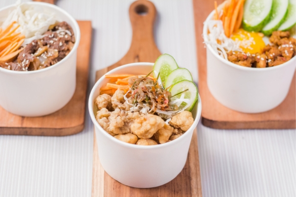 A wooden table set with a variety of healthy rice bowls, each filled with colorful vegetables, lean proteins, and tropical ingredients, ready to be enjoyed in a casual, refreshing setting.