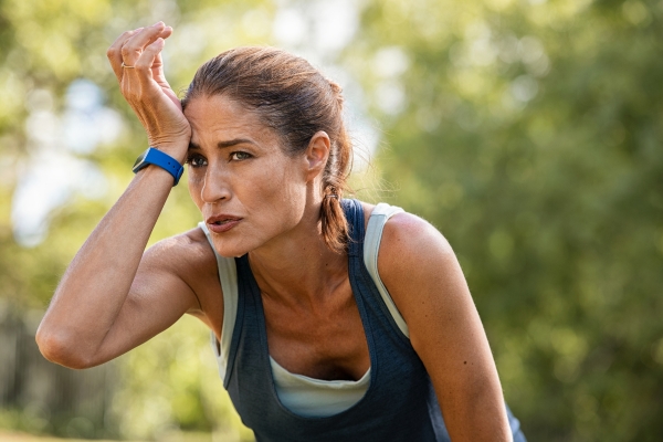 A runner wiping sweat from their face during a sunny morning jog on a tropical path, surrounded by lush greenery, capturing the heat and humidity of Borneo’s climate.